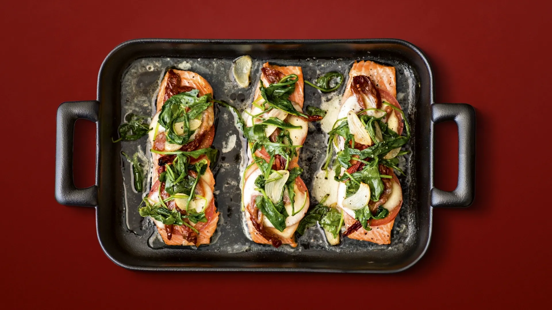 A photograph of a delicious oven tray with roasted salmon, tomatoes, garlic, spinach and sun dried tomatoes.